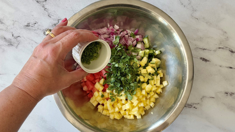 Hand holding small bowl of lime zest over bowl of unmixed fruit salsa