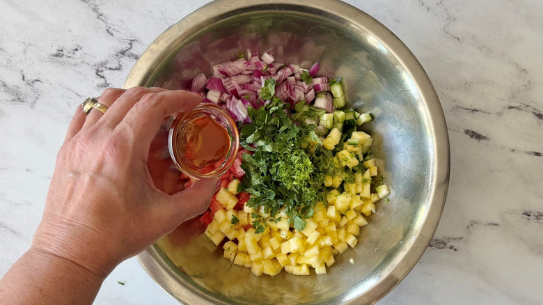 Hand holding small bowl of honey over bowl of unmixed fruit salsa