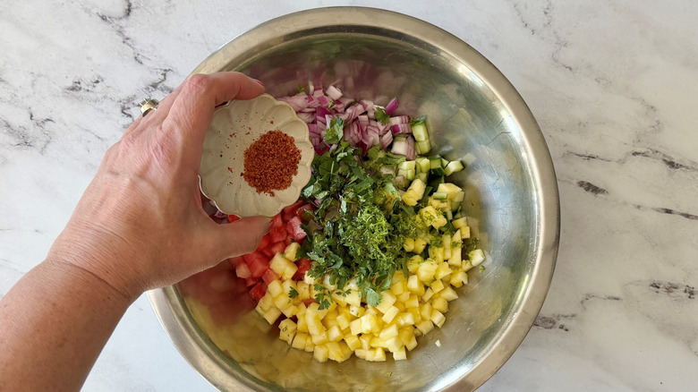 Hand holding small bowl of Tajín over bowl of unmixed fruit salsa