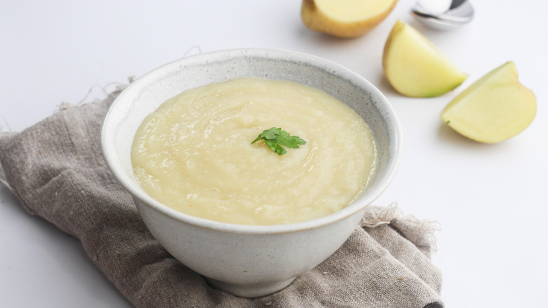 bowl of potato soup next to potato and spoon