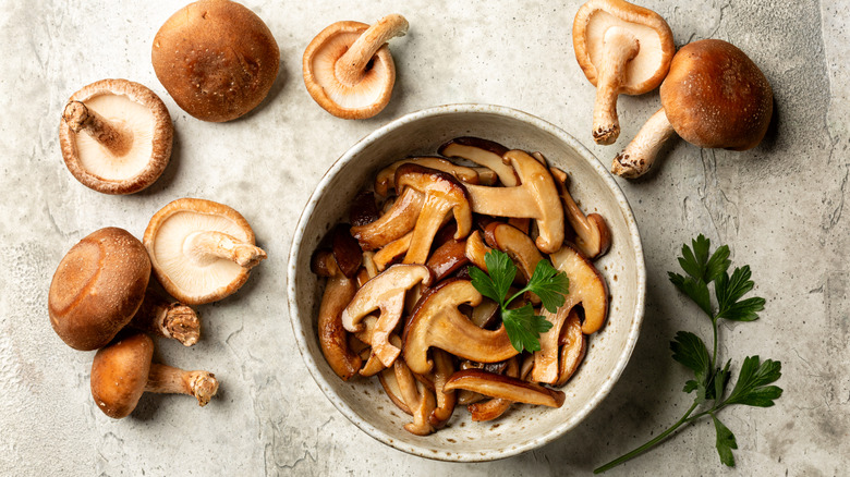Cooked mushrooms in a bowl next to raw mushrooms