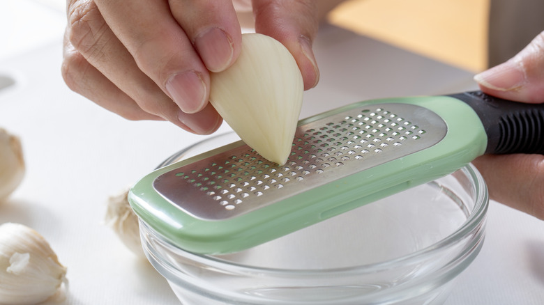 A cook grating garlic into a glass bowl