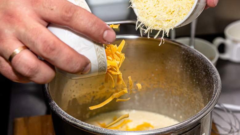 A cook dumping cheese into sauce