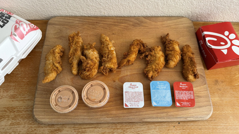Tenders and sauces from Raising Cane's and Chick-fil-A on a cutting board with their boxes to the side