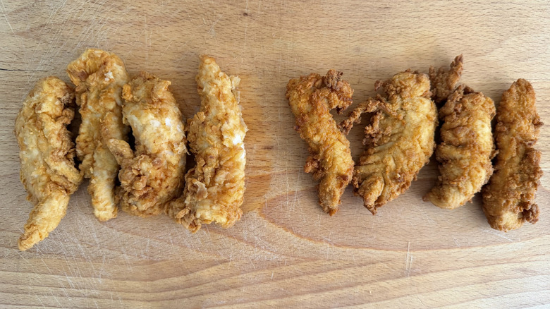 Four chicken tenders from Raising Cane's and Chick-fil-A grouped together on a cutting board