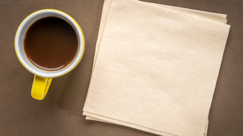 A cup of coffee beside a stack of paper napkins.