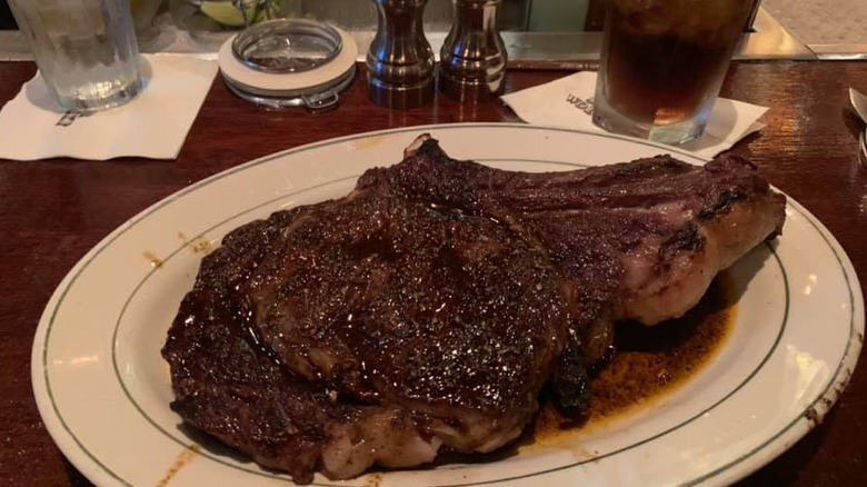 Smith & Wollensky ribeye on a plate ine front of seasonings and a soda in a glass cup