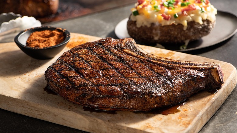 LongHorn Steakhouse outlaw ribeye steak on a board next to a baked potato and spices