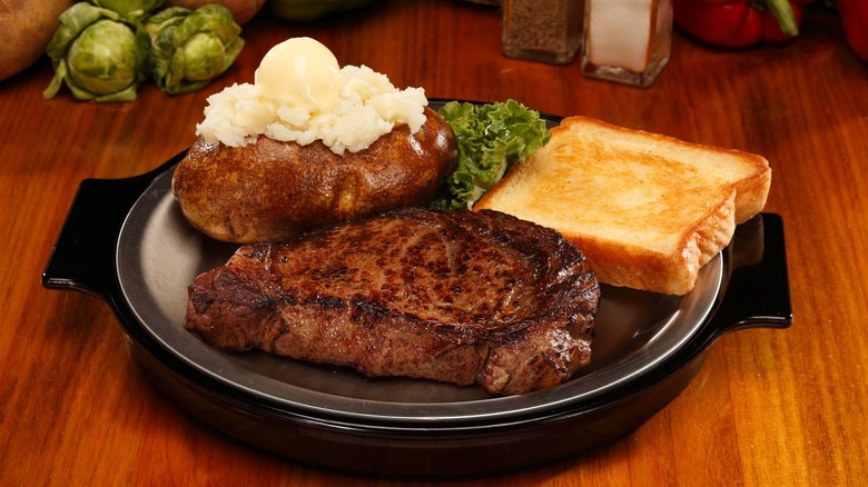 steak on a skillet plate with a baked potato and toast