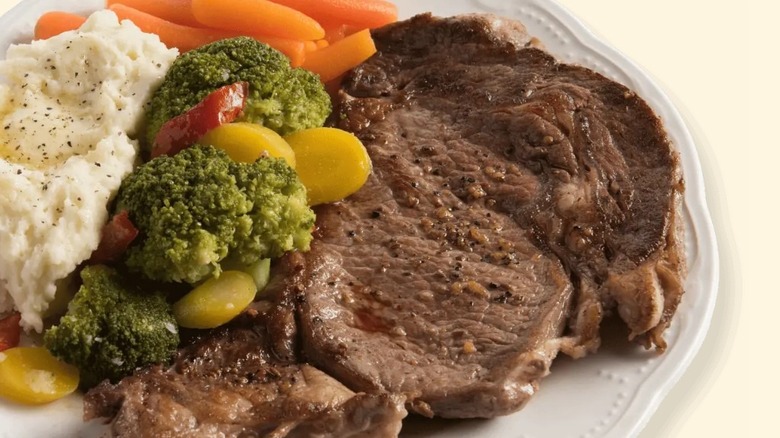 a steak sits next to vegetables and mashed potatoes