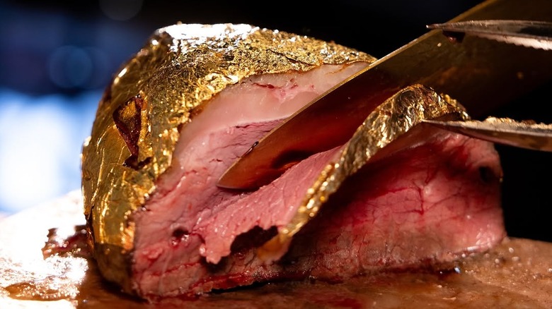 knife slices through a large steak covered in edible gold