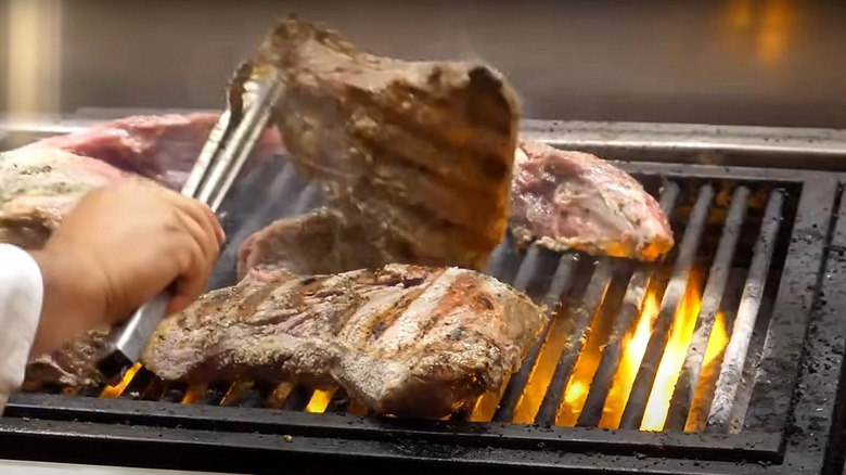 cook uses tongs to turn over steak on grill