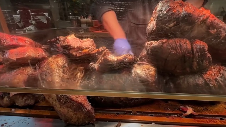 cook prepares food from behind a mound of assorted meats at a grilling station