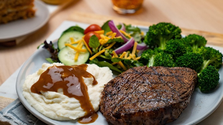 sirloin steak sits next to mashed potatoes, salad, and broccoli