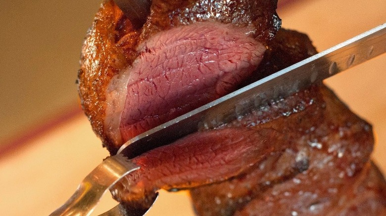 knife slicing steak held by tongs