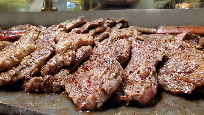 several steaks sit on a flat grill