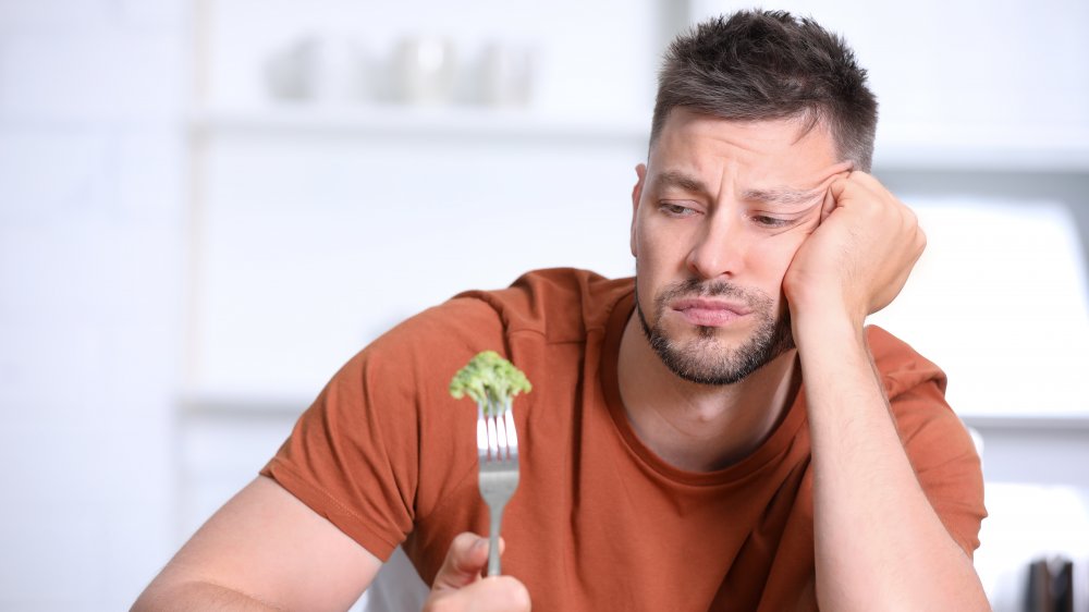 Disappointed man eating broccoli