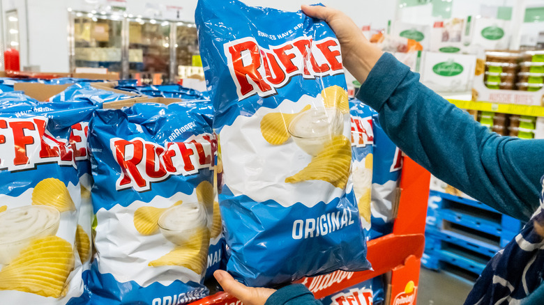 A person holding a bag of blue Ruffles