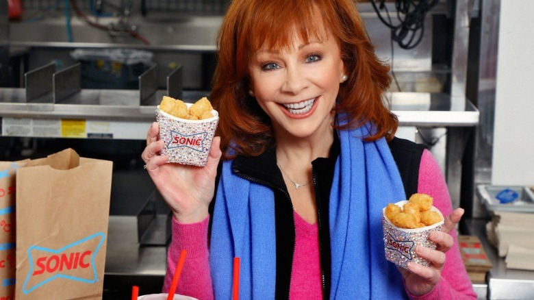Reba McEntire holding containers of Sonic tater tots and smiling