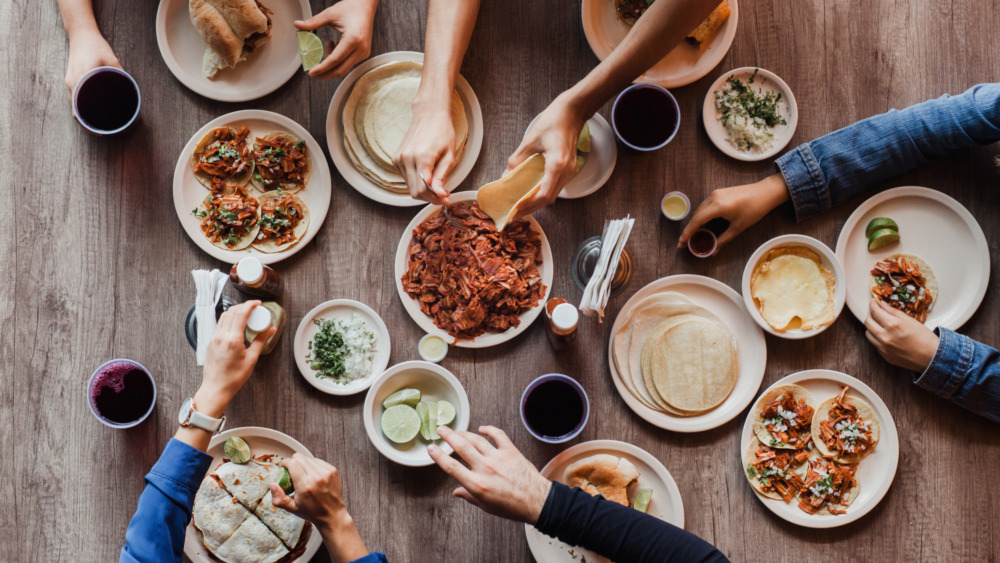 Hands making tacos around a table