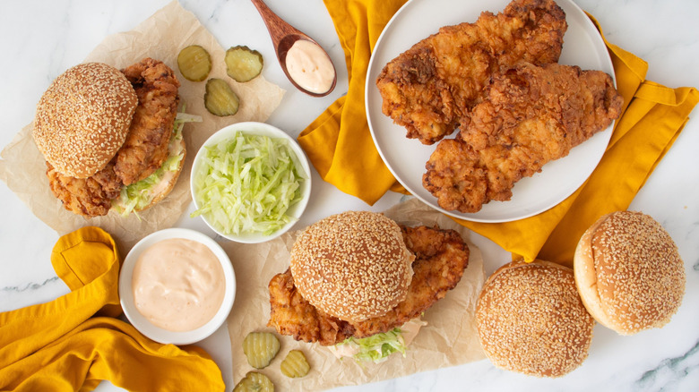 Various fried chicken sandwiches with toppings and pieces of fried chicken
