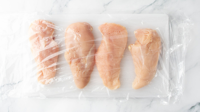 Raw chicken breasts covered with plastic wrap