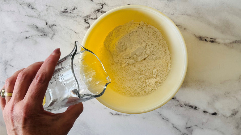 Hand pouring water into tempura mix in bowl