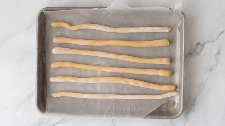 long, irregular marzipan cylinders on a wax paper-covered pan