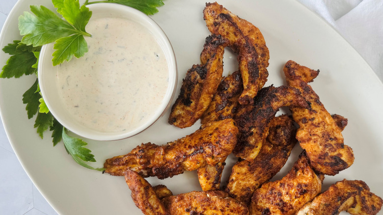 chicken strips on an oval white plate with a bowl of white sauce