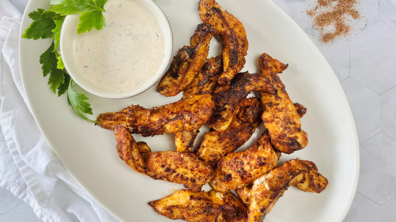 chicken strips on an oval white plate with a bowl of white sauce