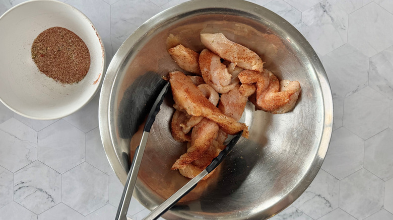 bowl of raw chicken with tongs