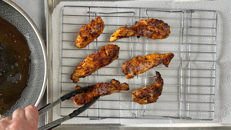 hand holding chicken strip with tongs over a wire rack