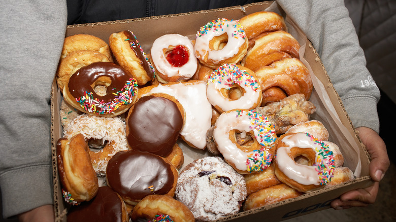 Person holding large cardboard box of doughnuts