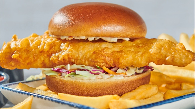 A fish burger on top of fries.