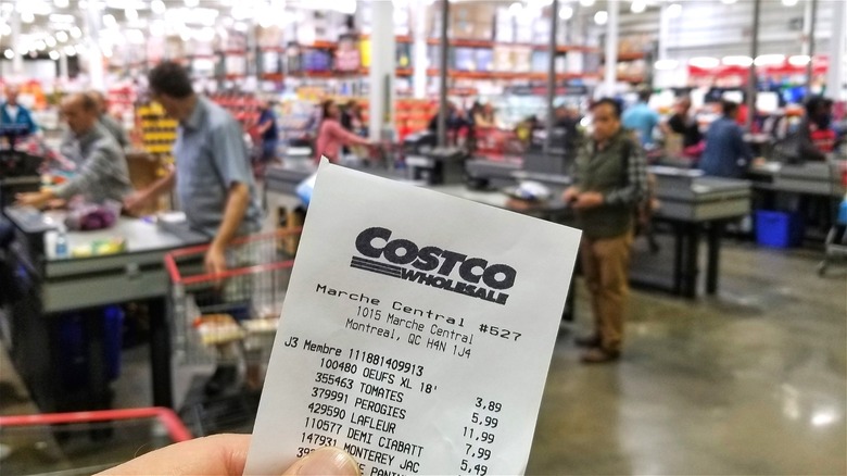 Hand holding Costco receipt in front of checkout lanes