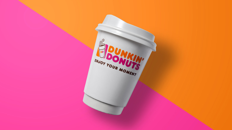 A Dunkin' coffee cup over a pink and orange background