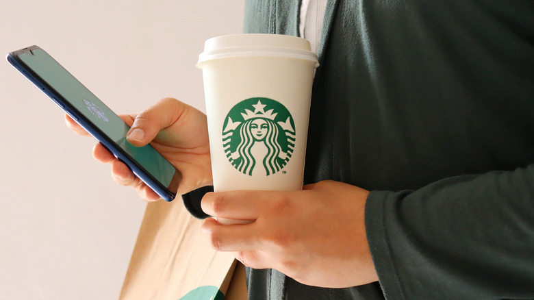 Person holds Starbucks cup and phone