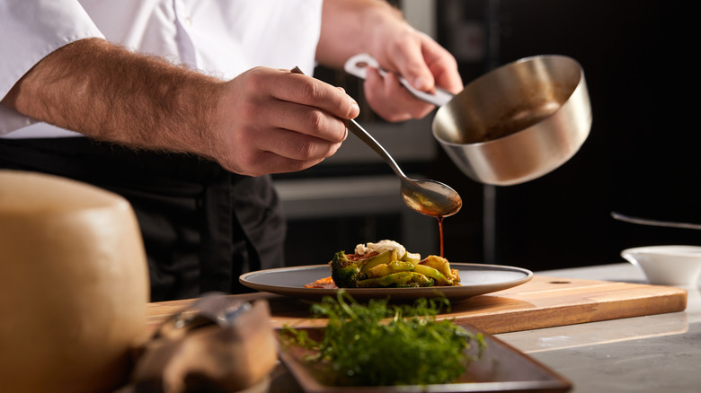 Chef drizzling sauce on gray plate