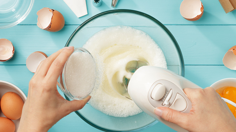 Mixing sugar into egg whites surrounded by egg shells