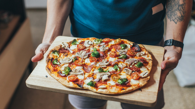 Person holding pizza on wooden cutting board