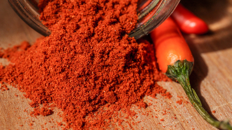 Hungarian paprika powder spilling out of a jar onto a cutting board next to a red pepper