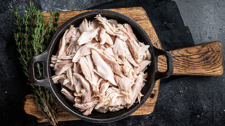 Pulled, shredded cooked rotisserie chicken in a cast iron skillet on a cutting board with sprigs of thyme to the side.