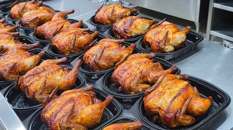 Rows of hot, golden brown rotisserie chickens in plastic containers, ready to be packaged with a top and sold at a grocery store.