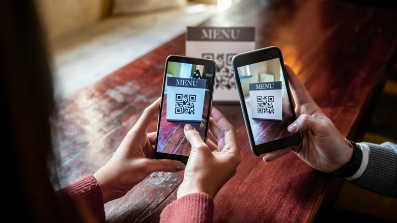 Two people scanning a QR code menu with their phones at a restaurant
