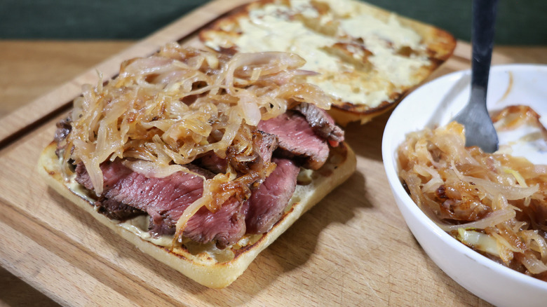 ciabatta roll topped with sliced rare, caramelized shallots, and Dijonnaise sitting on cutting board next to bowl of caramelized shallots