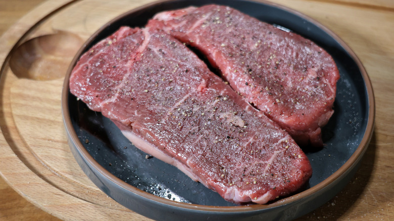 two raw sirloin steaks seasoned with salt and pepper on a plate