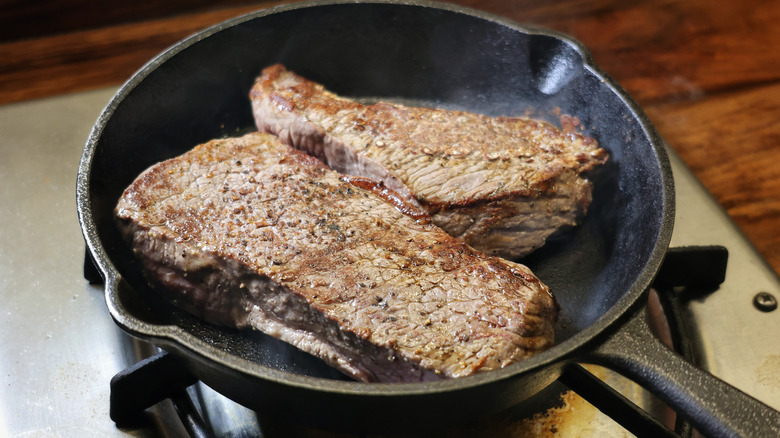 two seared sirloin steaks in a small cast iron pan