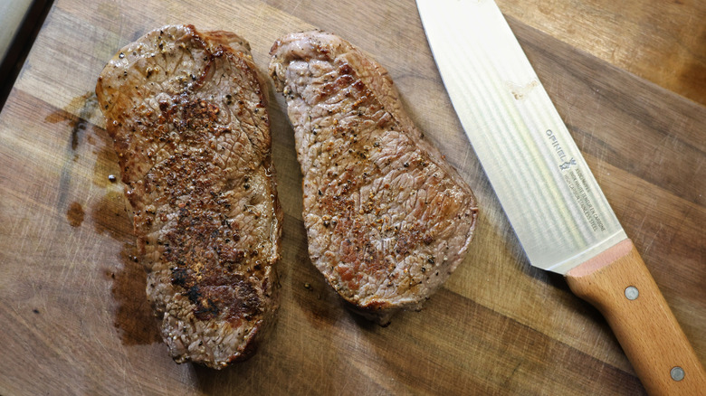 two cooked sirloin steaks on a cutting board next to a chef's knife