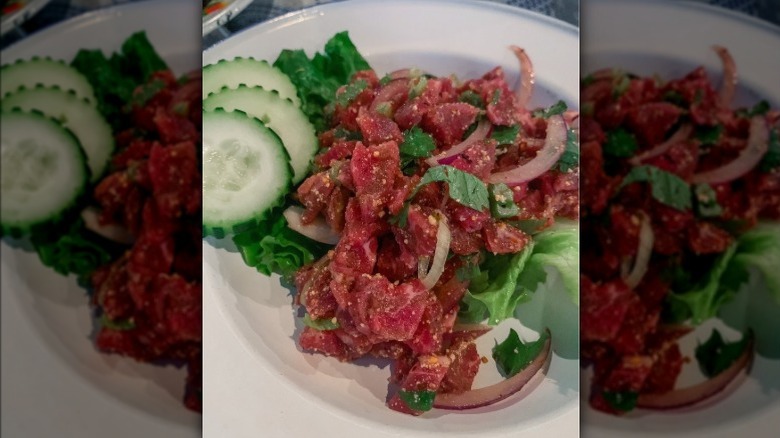 Thai dish goi neur, a raw meat salad with onions and cucumbers on a white plate