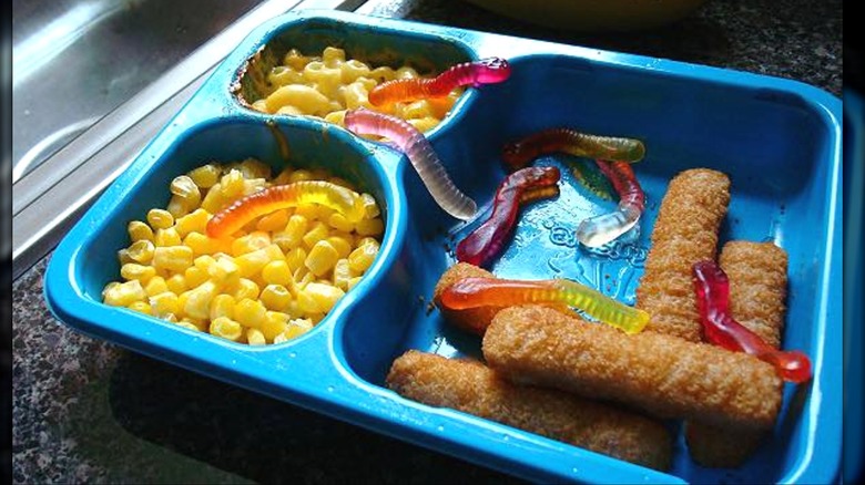 Fish sticks with gummy worms, corn, and macaroni and cheese in a blue Kids Cuisine TV dinner tray